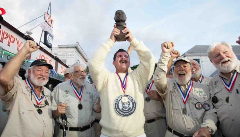 Surrounded by previous winners of the Hemingway Look-Alike Contest, 2026 champion Chris Dutton hoists his trophy, a bronze bust of Nobel Prize-winning author Ernest Hemingway, outside Sloppy Joe’s Bar.